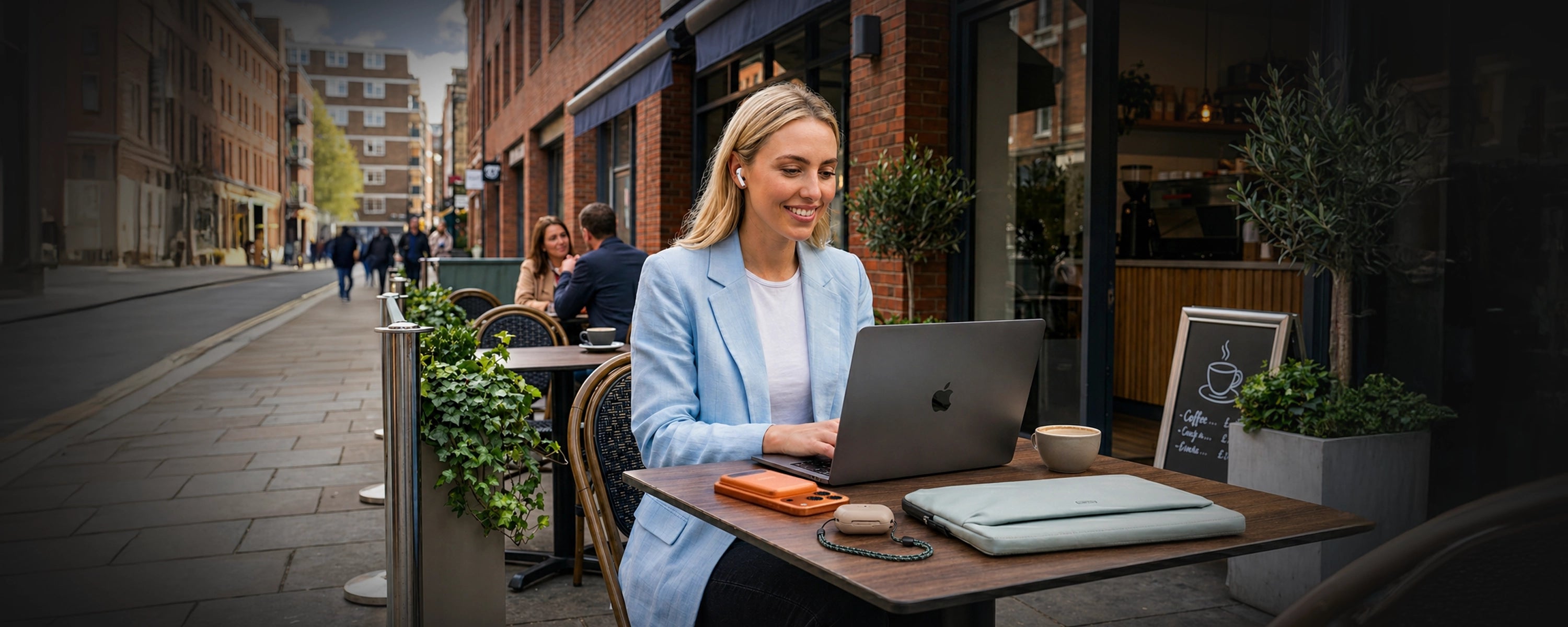 Woman using a laptop at an outdoor cafe table with a city street background